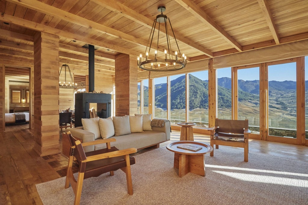 Traditional Bhutanese lodge with floor-to-ceiling windows perched on hillside, overlooking misty Phobjikha Valley and pine forests at sunset