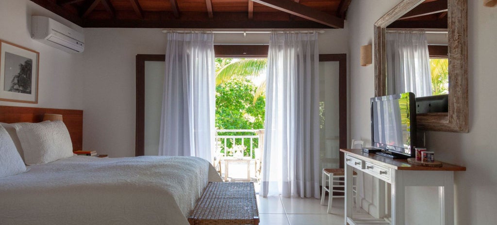 Luxurious Brazilian farmhouse suite with elegant wooden furnishings, plush white bedding, and warm tropical lighting in a spacious, serene interior