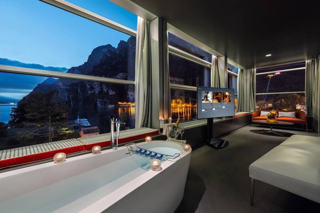 Elegant sky-blue luxury suite with panoramic mountain views, plush king bed, modern Italian design, and floor-to-ceiling windows overlooking scenic landscape