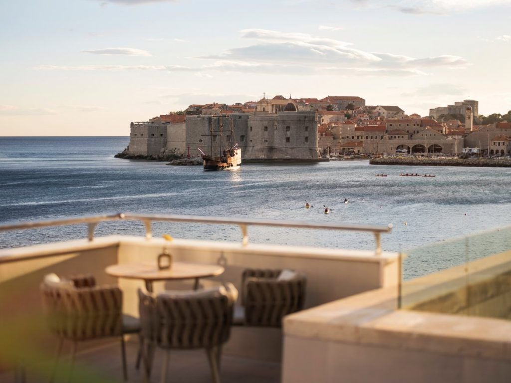 Opulent seaside hotel with stone facade and curved balconies overlooking the Adriatic Sea, surrounded by palm trees at dusk