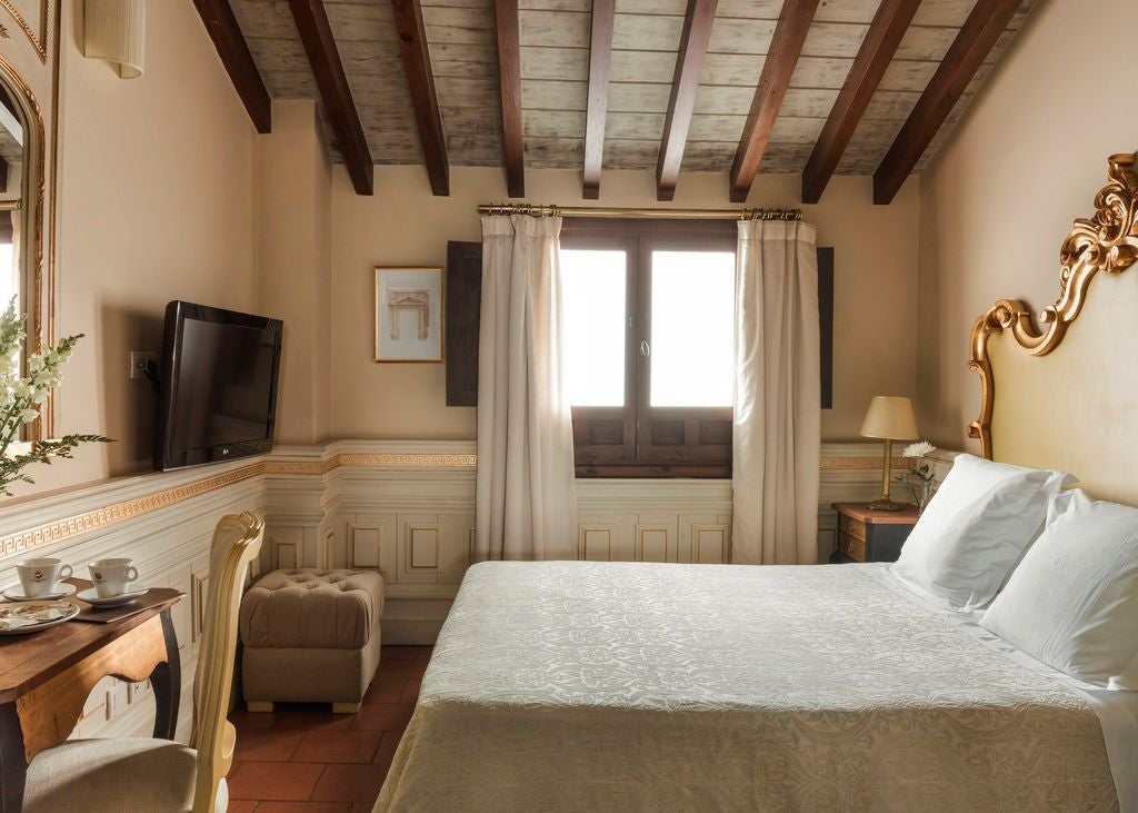 Elegant Spanish colonial hotel room with ornate wrought iron bed, crystal chandelier, traditional tile floors and white gauze drapes