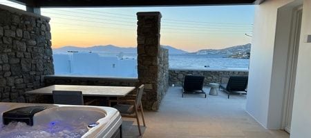 Luxurious one-bedroom suite overlooking the Aegean Sea, featuring a private hot tub and minimalist white Cycladic design in Mykonos, Greece.