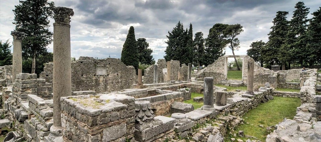 Ancient Roman ruins of Salona with well-preserved stone columns and archways amid lush Mediterranean greenery at sunset