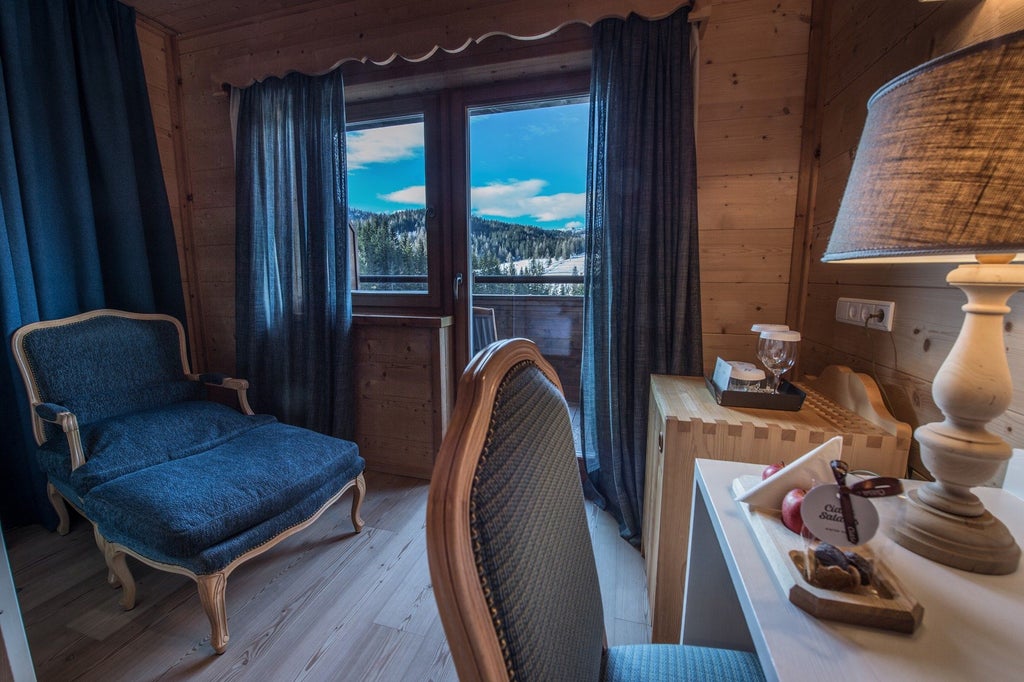 Elegant alpine hotel room with exposed wooden beams, modern furnishings, plush bed, and expansive mountain views through panoramic windows