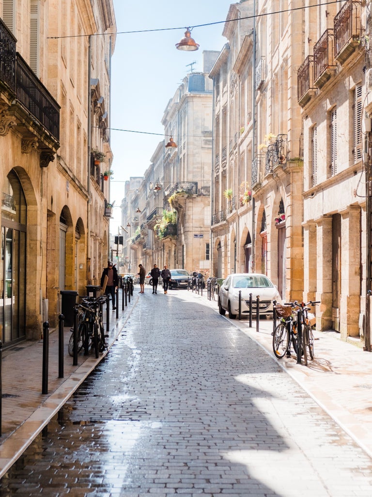 Elegant 19th-century limestone buildings with wrought-iron balconies line a charming cobblestone street in historic Bordeaux, France