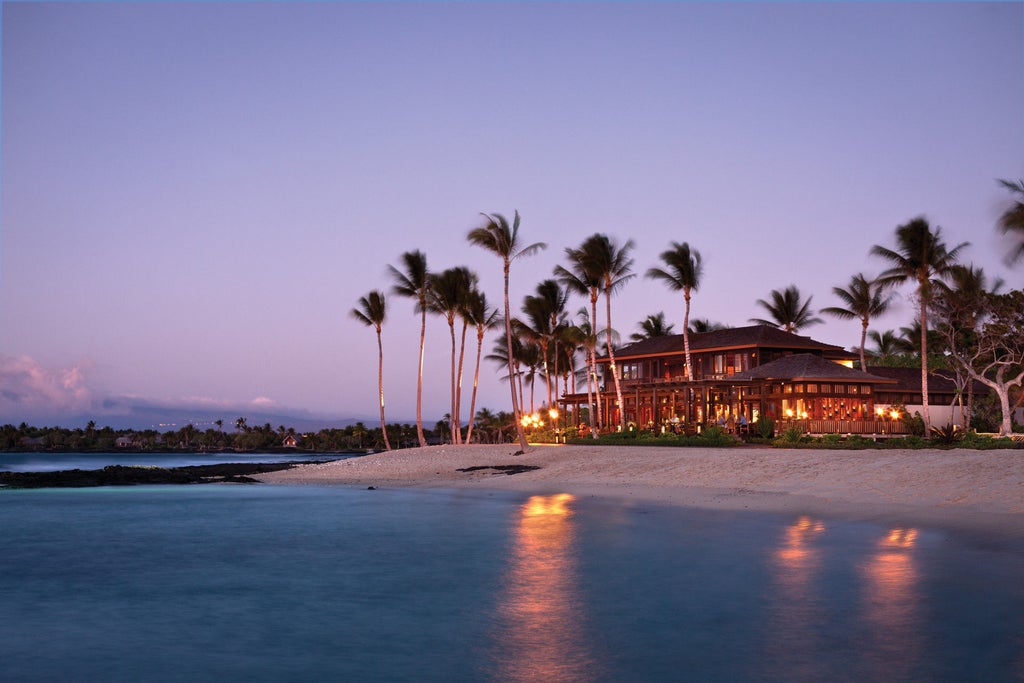 Luxury beachfront hotel with infinity pool overlooking Pacific Ocean, swaying palm trees and elegant lounge chairs at sunset in Hawaii