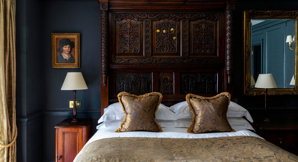 Elegant hotel room with ornate period furnishings, soft cream walls, vintage artwork, plush king bed with decorative headboard at Batty Langley's boutique accommodation