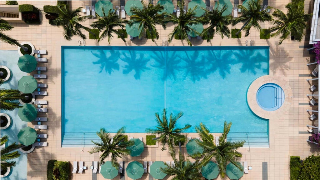 Luxurious glass-and-steel Four Seasons hotel tower rising above vibrant Miami skyline, gleaming with modern architectural elegance and tropical blue sky backdrop