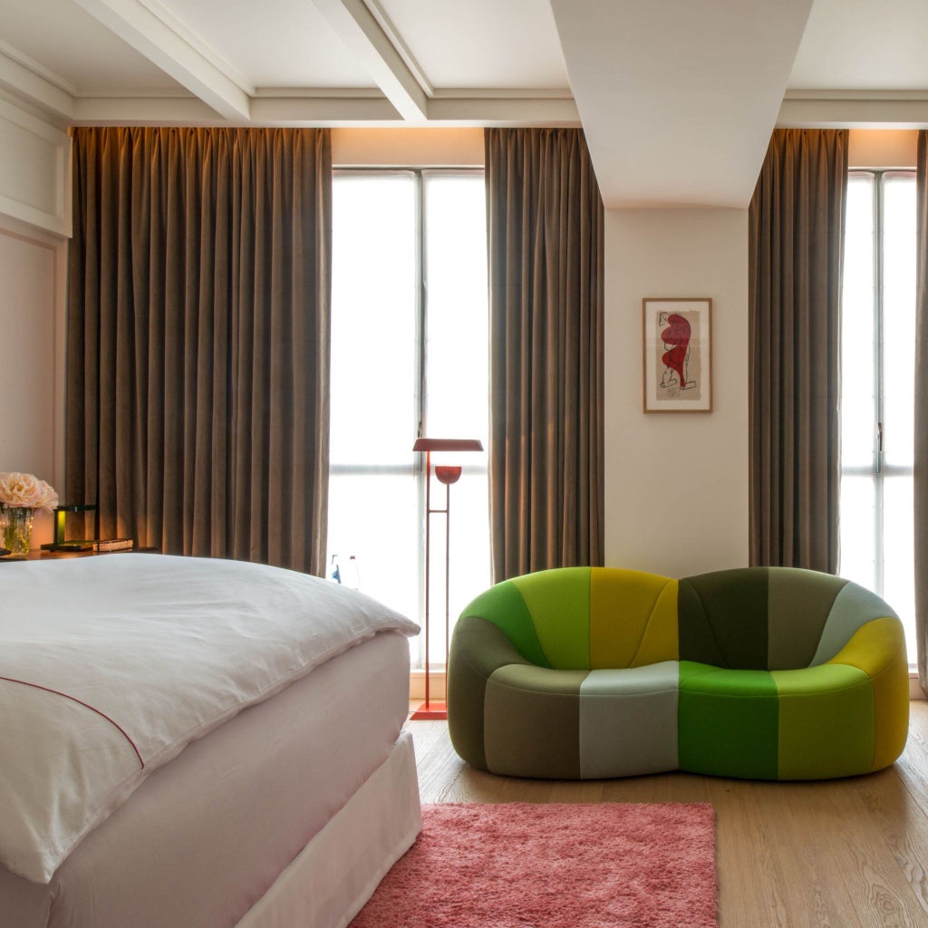 Luxurious executive hotel room at Sinner Paris, featuring elegant dark wood furnishings, plush bed, and moody atmospheric lighting with sophisticated French design elements