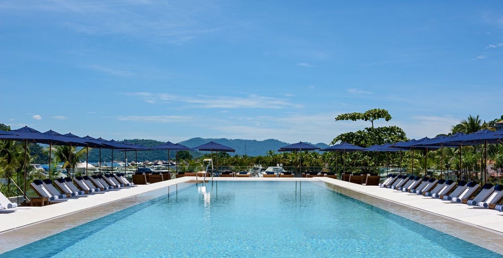 Elegant seaside resort with infinity pool overlooking turquoise bay, surrounded by lush mountains and luxury yacht marina in Brazil