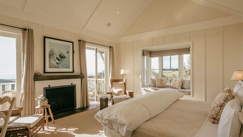 Elegant suite featuring rustic wood beams, plush king bed, stone fireplace, panoramic ocean views and private balcony with lounge seating