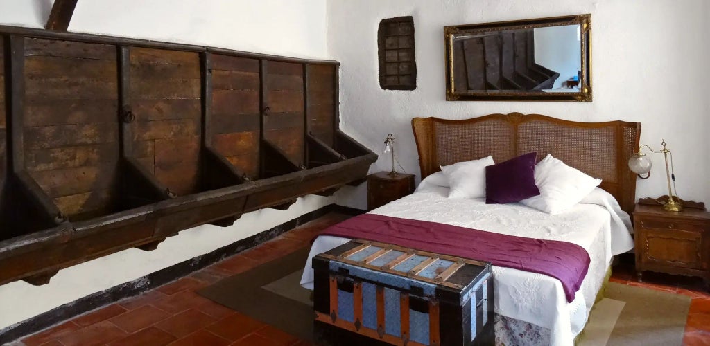 Luxurious rustic Spanish hotel room with exposed wooden beams, elegant white linens, and traditional stone wall at Cortijo del Marqués estate