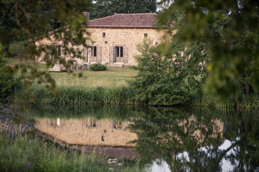 Luxurious French countryside cottage bedroom with elegant wooden furnishings, soft natural light, and panoramic views of rolling green landscape at Domaine des Etangs