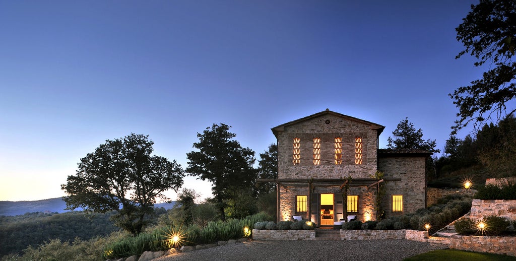 Luxurious Italian castle-turned-hotel with stone facade, ornate windows and arched entrance, set against rolling Umbrian countryside