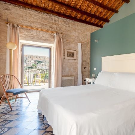 Elegant Italian boutique hotel room with minimalist design, soft neutral palette, rustic stone wall, and warm wooden furnishings at Casa Talía in Siracusa