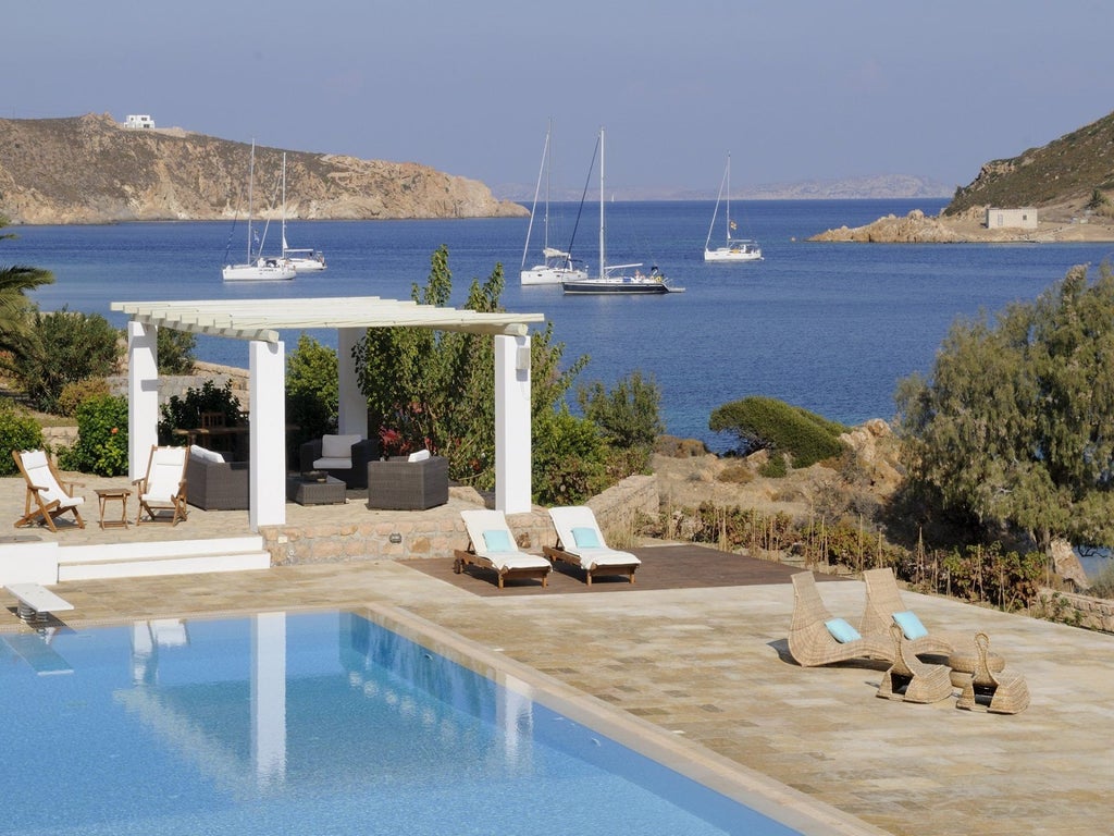 Elegant stone villa with terracotta roof overlooking azure Aegean Sea, surrounded by lush Mediterranean garden and traditional Greek architectural design