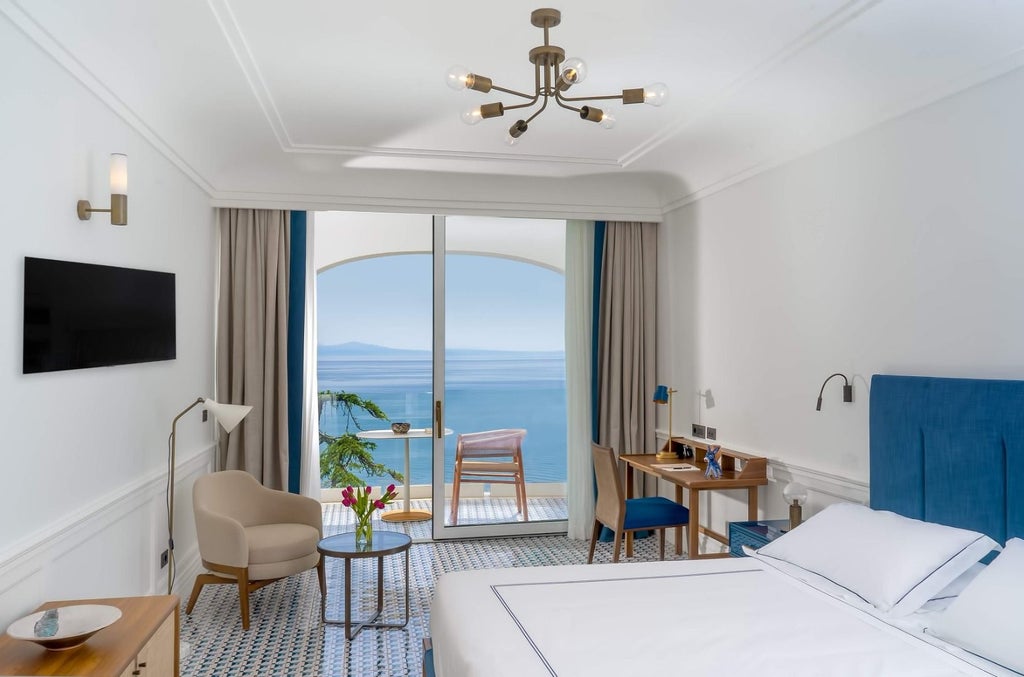 Elegant white Mediterranean hotel room with balcony overlooking Amalfi Coast, featuring plush bedding and modern coastal decor