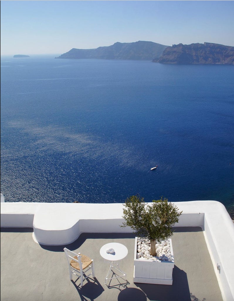 Luxurious white-washed hotel suites cascade down Santorini's caldera cliff, featuring infinity pools and terraces overlooking Aegean Sea