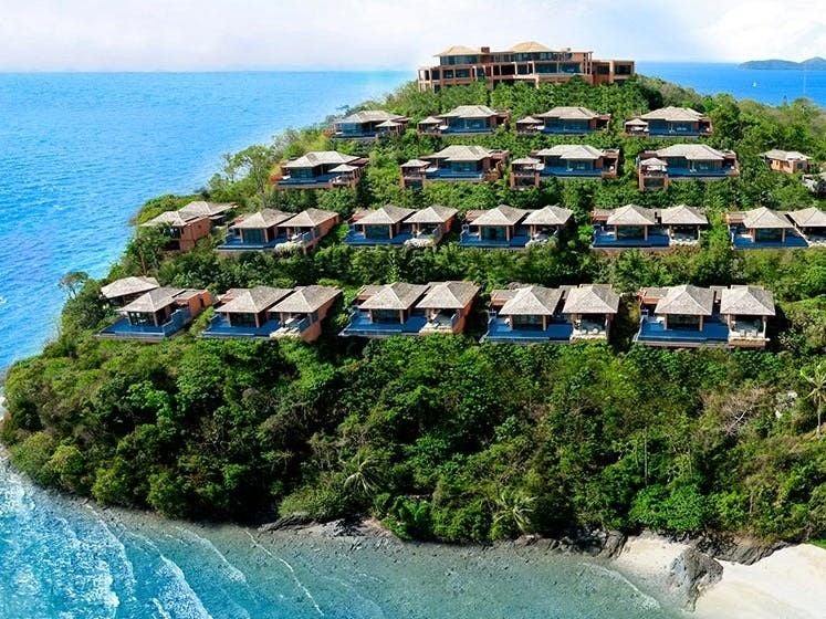 Luxurious infinity pool overlooking turquoise Andaman Sea at sunset, with modern pavilions nestled among tropical greenery in Phuket