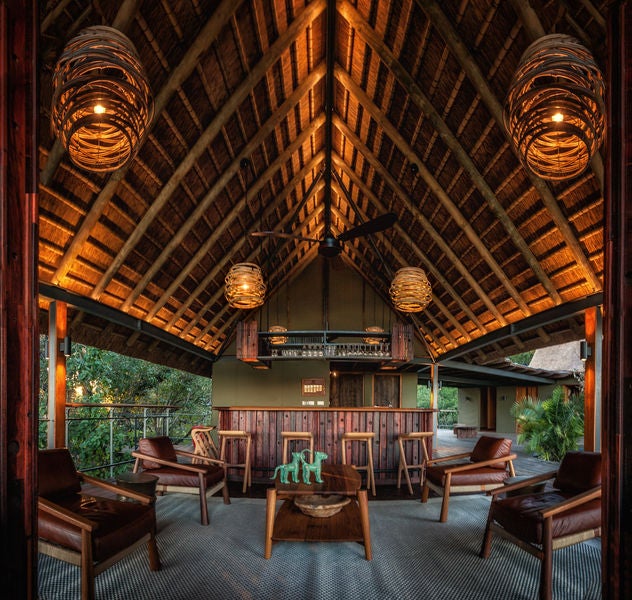 Safari lodge perched on raised wooden deck over savanna, featuring thatched roof and private pool overlooking grasslands at dusk