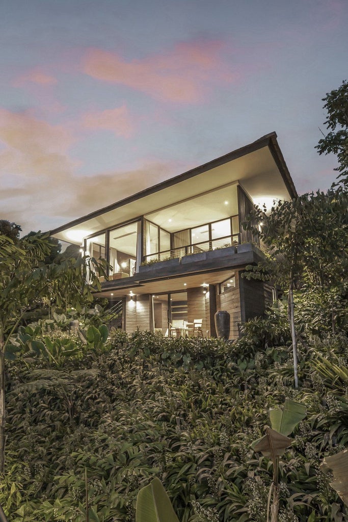 Luxurious two-bedroom cabin suite with contemporary wood interiors, floor-to-ceiling windows overlooking lush Indonesian rainforest views