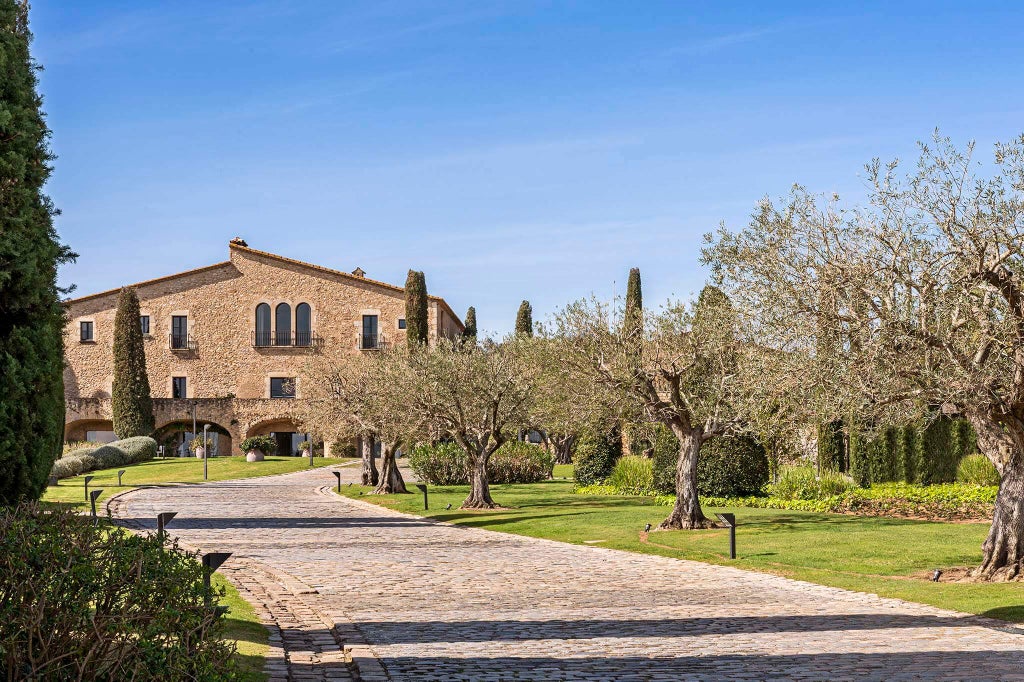 Elegant stone manor hotel set in verdant Spanish countryside with manicured gardens, terra-cotta roof tiles and luxury pool terrace