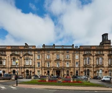 Elegant exterior of a luxurious hotel with grand architecture, featuring cream-colored facade, ornate windows, and manicured landscaping in a historic UK setting