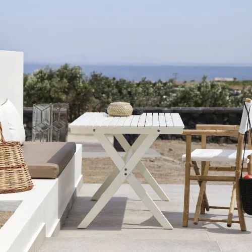 Luxurious Grecian villa bedroom with stone walls, wooden furnishings, and a private balcony overlooking scenic Santorini landscape at sunset