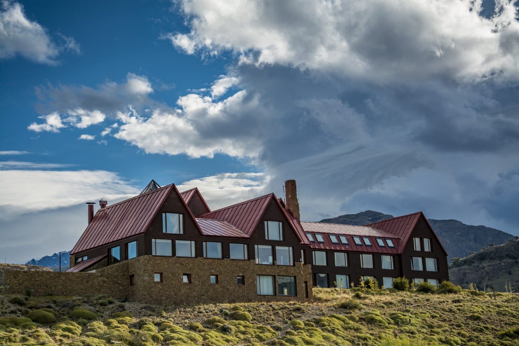 Elegant mountain lodge with stone facade and wood accents nestled in snow-capped Andes peaks, featuring expansive panoramic windows