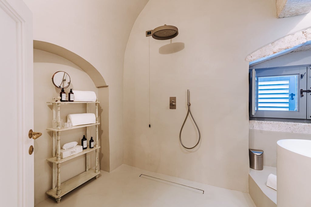 Elegant boutique hotel room with plush white bedding, vintage terracotta floors, and large windows overlooking Italian architecture in Puglia