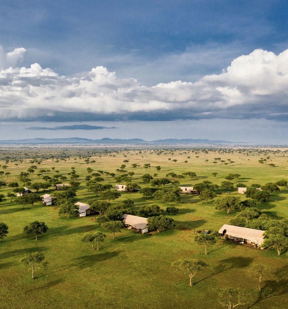 Luxurious safari tent with canvas walls and wooden deck overlooking vast Serengeti grasslands at sunset, antique furnishings visible inside