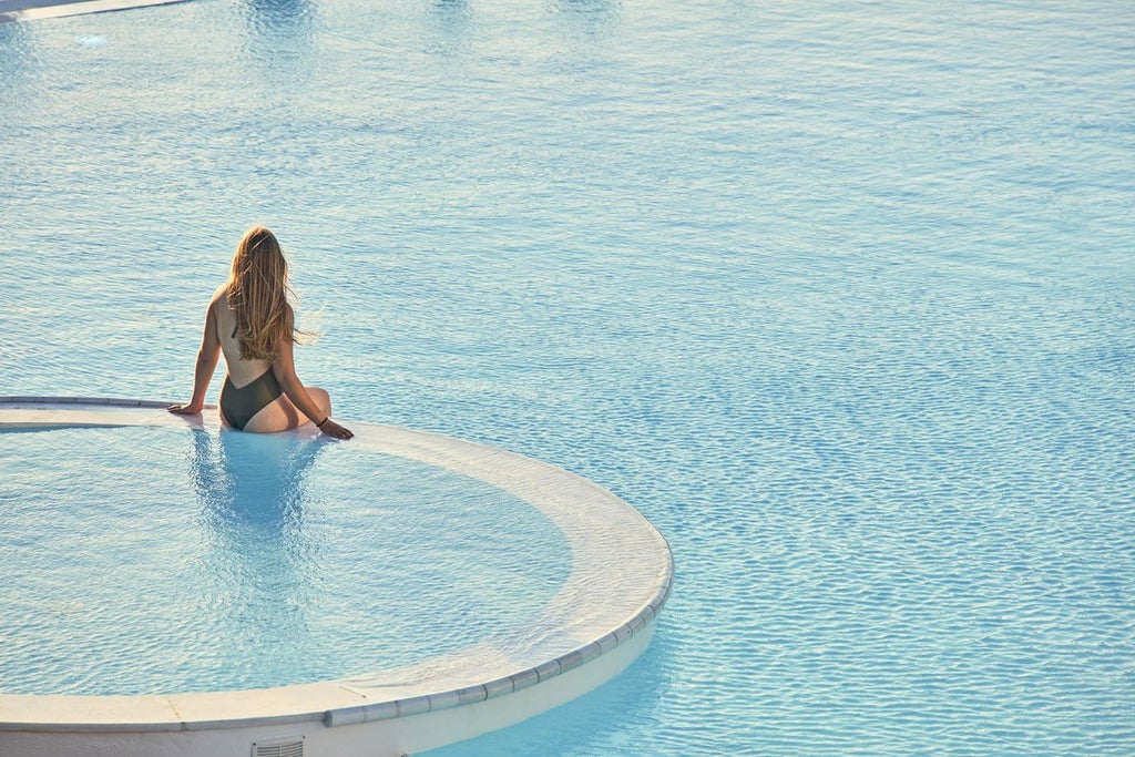 A luxurious infinity pool overlooking the Aegean Sea and Ios coastline, with elegant white loungers and traditional Greek architecture