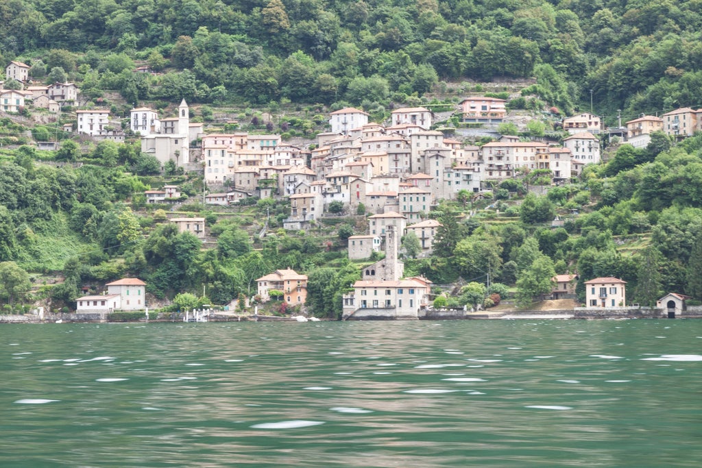 Aerial view of Lake Como's turquoise waters surrounded by luxury villas, cypress trees, and snow-capped Alps in northern Italy