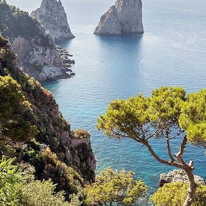 Elegant white hotel with terracotta tiled roof overlooking scenic Italian coastline, featuring stone balconies and lush Mediterranean gardens at sunset