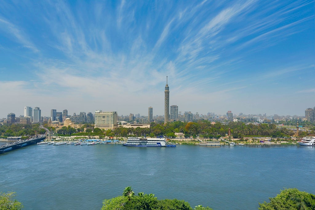 Elegant Nile Ritz-Carlton hotel towers over Cairo skyline, featuring grand columns, palm-lined driveway and golden evening lighting