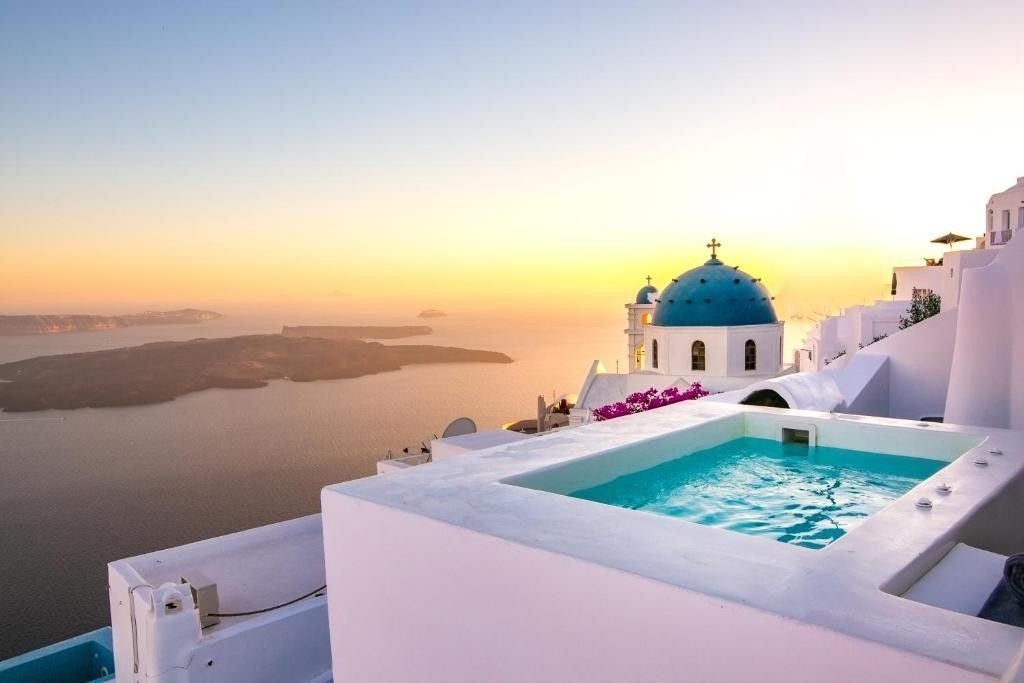 Elegant white Mediterranean suite with private infinity pool overlooking Aegean Sea, featuring minimalist outdoor loungers at sunset