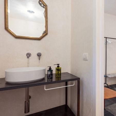 Rustic chic hotel room in Sicilian stone house, warm terracotta tones, minimalist furnishings, arched window overlooking scenic landscape at Casa Talía