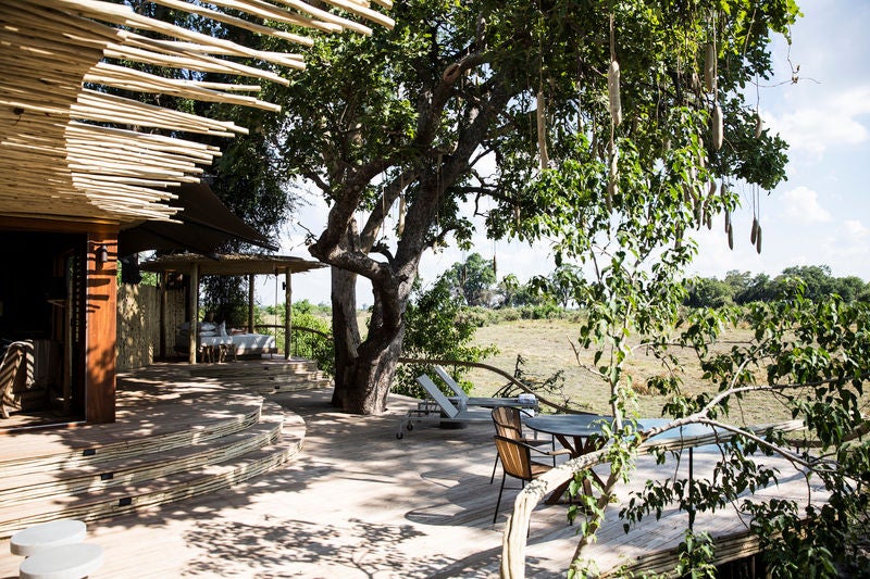 Elevated luxury safari tent perched on wooden stilts overlooks vast Botswana savanna, featuring private deck and canvas awnings