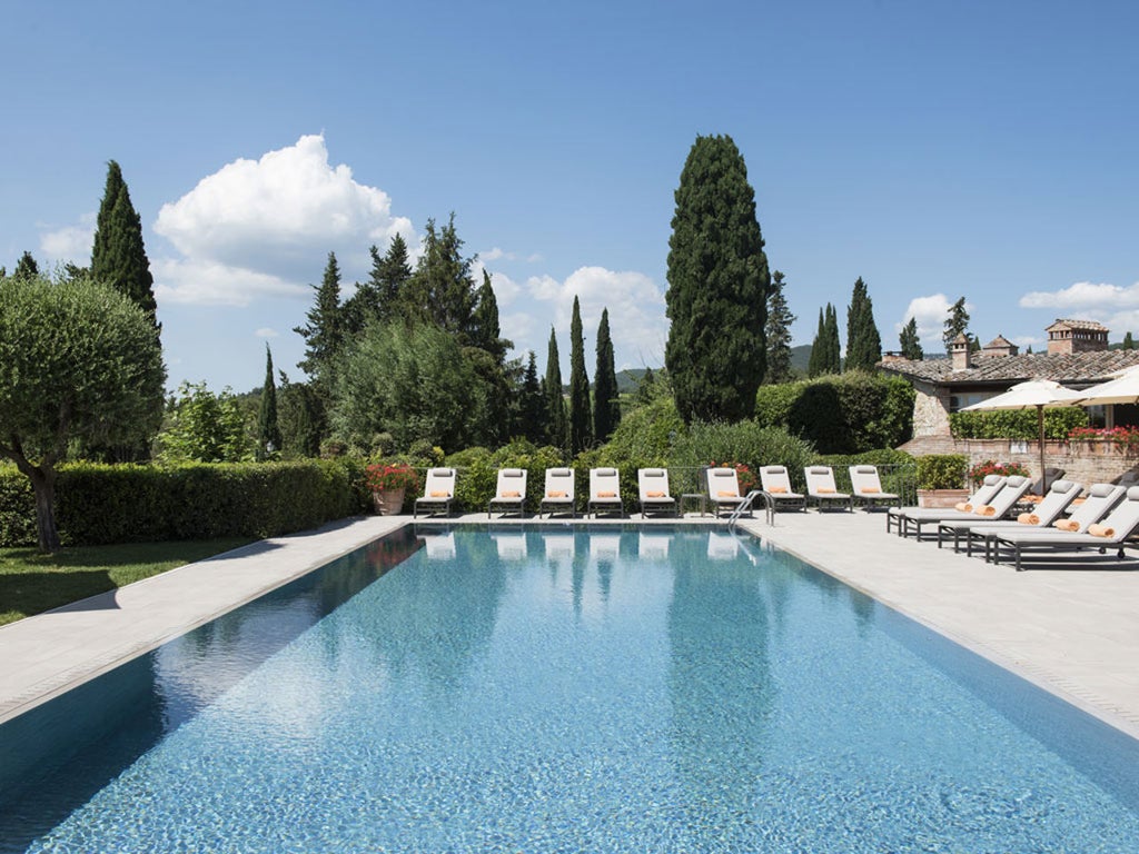 Elegant Tuscan luxury hotel set in ancient stone buildings surrounded by cypress trees and manicured gardens at golden hour