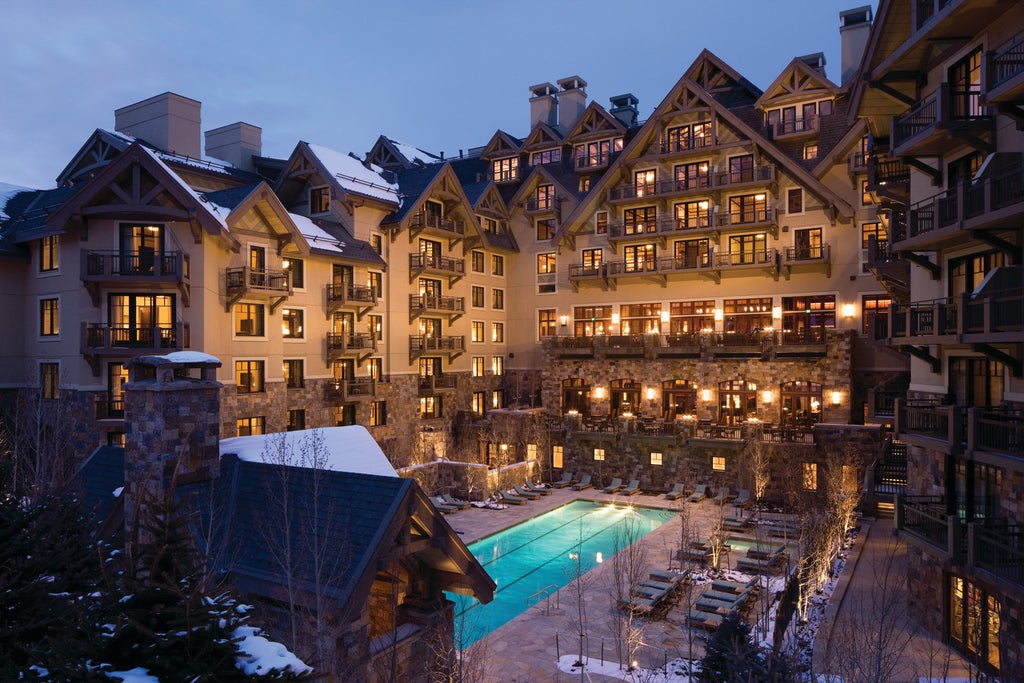 Luxurious mountain resort with stone facade, grand archways and snow-capped peaks behind, featuring elegant outdoor terrace seating