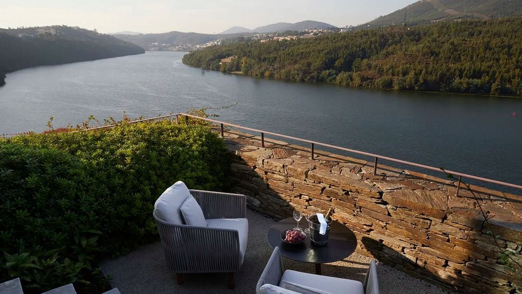 Modern resort hotel nestled in hillside vineyards overlooking Douro River, featuring infinity pool and panoramic valley views at sunset