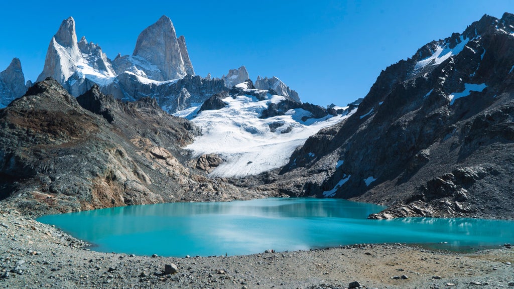 Mountain town of El Chalten nestled beneath dramatic snow-capped Fitz Roy peaks, with colorful alpine buildings along dirt roads at dusk