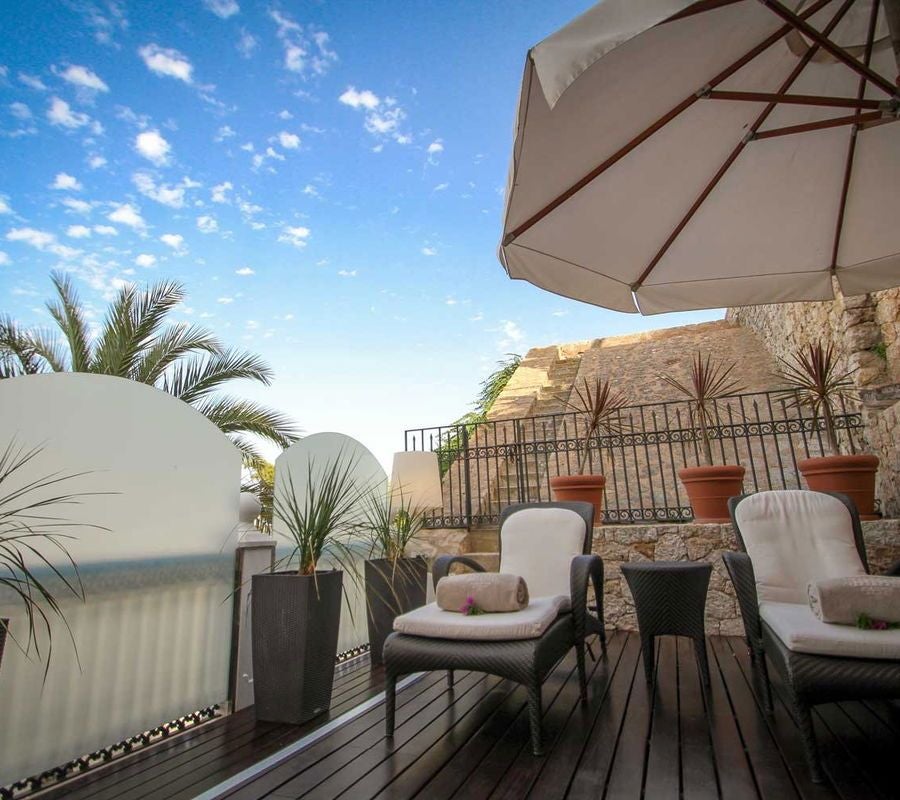 Luxurious stone exterior of historic hotel overlooking Dalt Vila's ancient walls, with warm Mediterranean lighting and elegant stone architecture