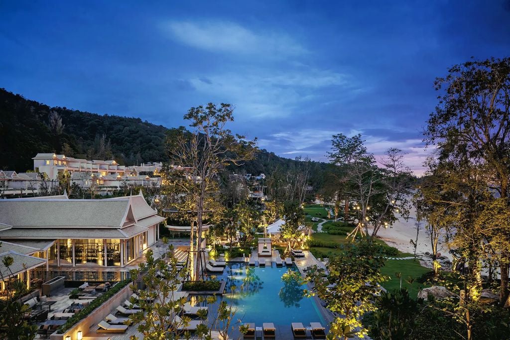 Luxurious oceanfront resort with infinity pool overlooking turquoise waters, palm trees and limestone cliffs of Phang Nga Bay