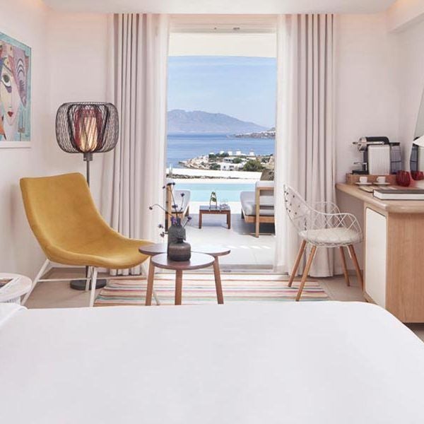 Elegant Aegean-style superior room with whitewashed walls, minimalist decor, and a breathtaking panoramic view of Mykonos' azure coastline and horizon.