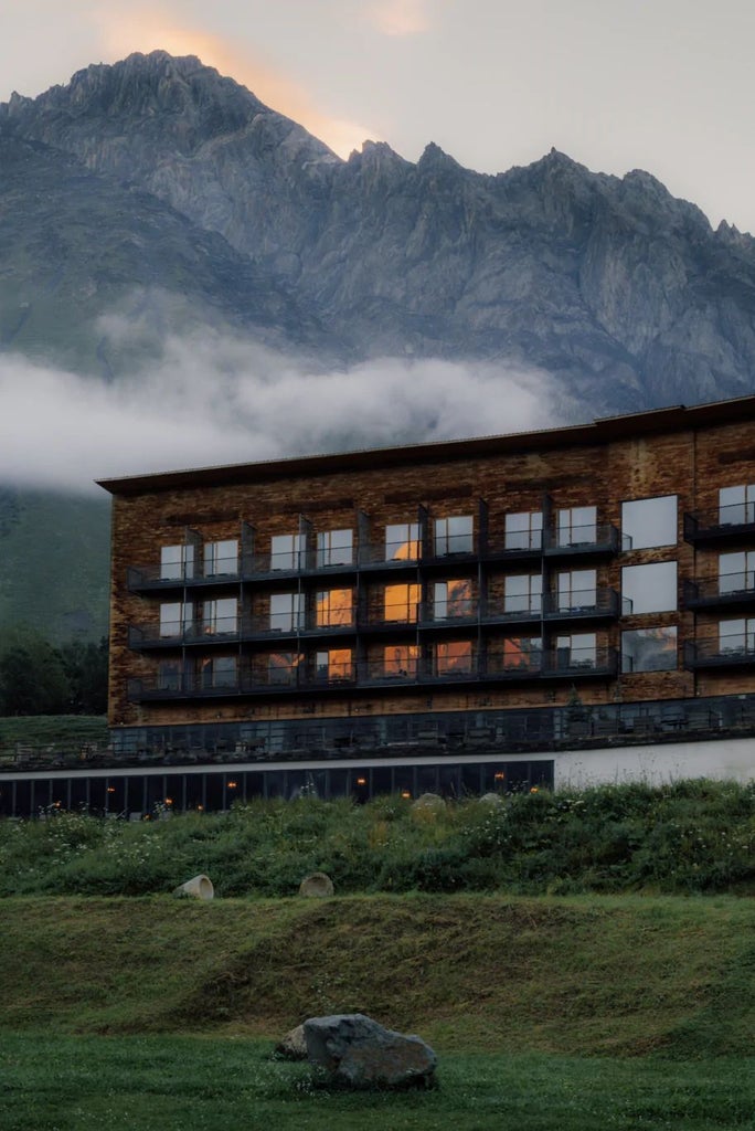 Luxurious mountain-view hotel room with modern minimalist design, large windows revealing dramatic Kazbegi mountain landscape, clean lines and natural light