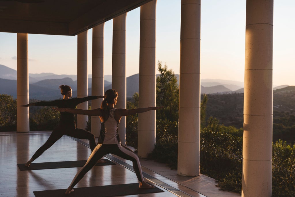 Elegant white pavilion with classical Greek columns overlooks infinity pool and Aegean Sea at sunset, surrounded by olive groves