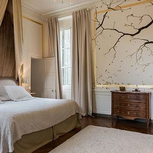 Elegant French château hotel room with antique furnishings, soft cream walls, ornate canopy bed, and delicate period-style chandelier in soft light