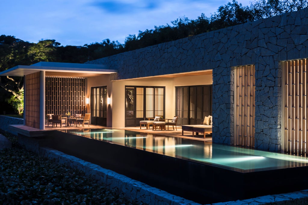 Infinity pool overlooking Vinh Hy Bay's turquoise waters, with luxury loungers and tropical forest-covered mountains in the distance