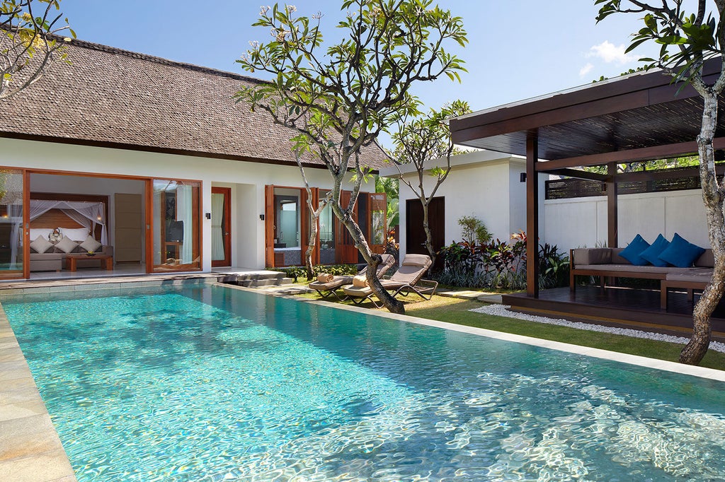 Luxurious infinity pool overlooking lush Balinese jungle valley at sunset, with traditional thatched-roof pavilions and tropical gardens